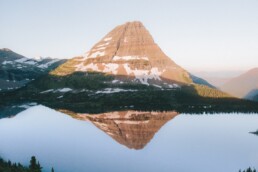 landscape photography of body of water surrounded by green trees beside mountain